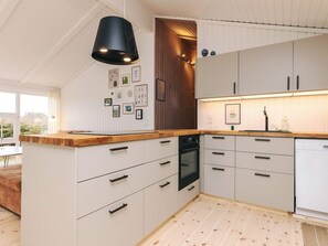 Una cocina moderna con armarios blancos, encimera de madera y lámpara colgante negra.