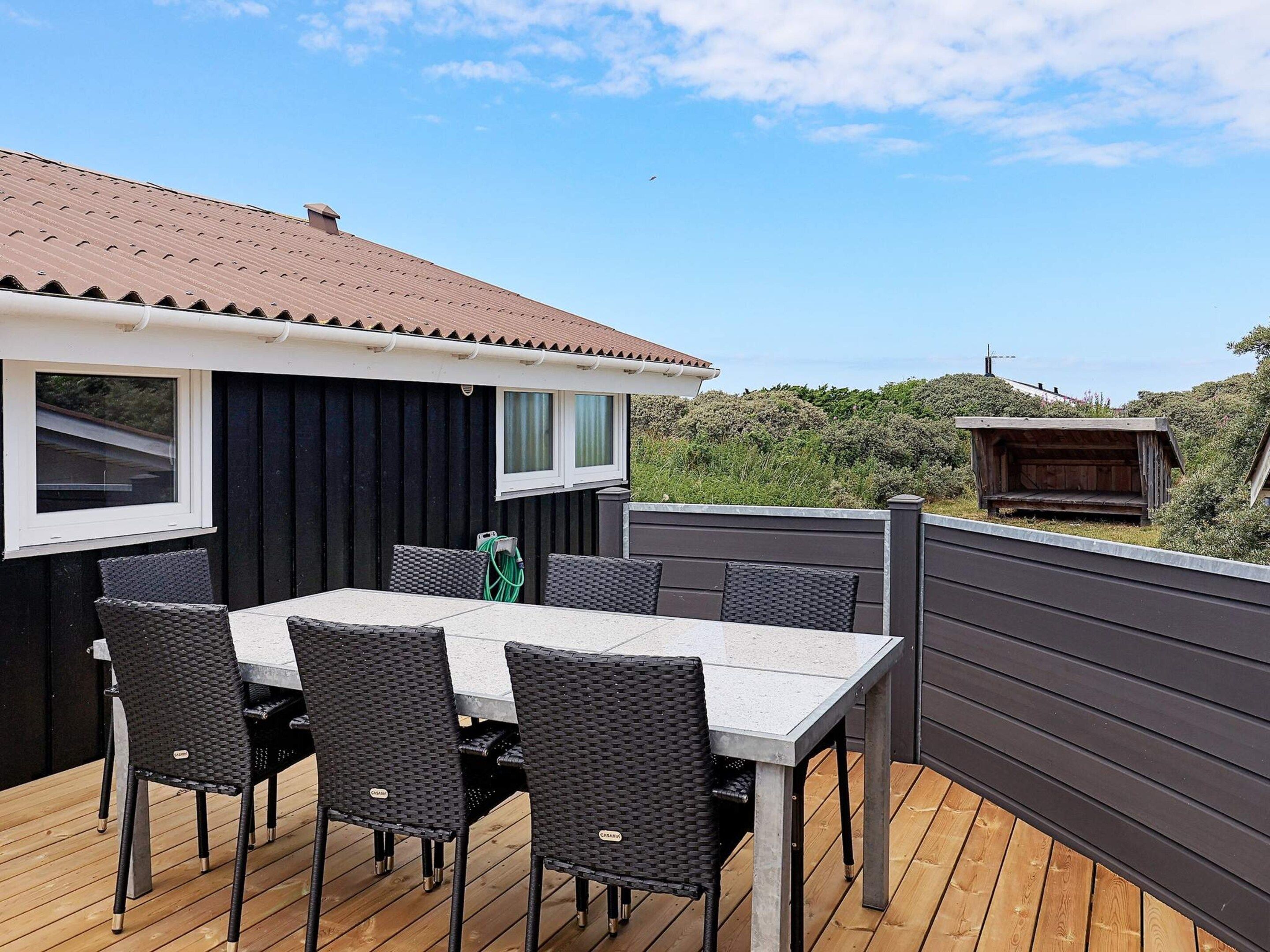 An outdoor deck with a table and chairs, a covered area, and a view of the surrounding landscape.