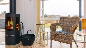 Una habitación acogedora con chimenea de leña, muebles de mimbre y vistas amplias a través de grandes ventanales.