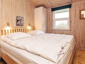 A wooden-paneled bedroom with a bed, a nightstand, a wall-mounted light, and a window. - 4 Star Holiday Home in Hjorring (Hjørring)