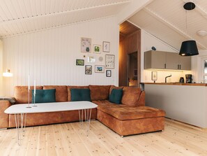 A modern living room with a brown sectional sofa, a white coffee table, and a kitchen area with a wooden countertop and cabinets. - 4 Star Holiday Home in Hjorring (Hjørring)