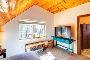 Ein Schlafzimmer mit Holzboden, einem großen Fenster mit Jalousien, einem Bett, einem Schreibtisch mit Fernseher und einer kleinen Bank.