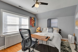Un dormitorio con cama, escritorio, silla, radiador y ventilador de techo.
