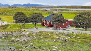A red house with a white picket fence, surrounded by green fields and mountains in the background. - 11 Person Holiday Home in Tarva (Orland)