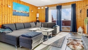 A modern living room with a wooden interior, a large sofa, a coffee table, and a view through a glass door. - 11 Person Holiday Home in Tarva (Orland)