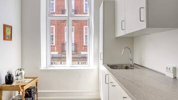 A kitchen with a window, a sink, cabinets, and a small wooden table with kitchen items.