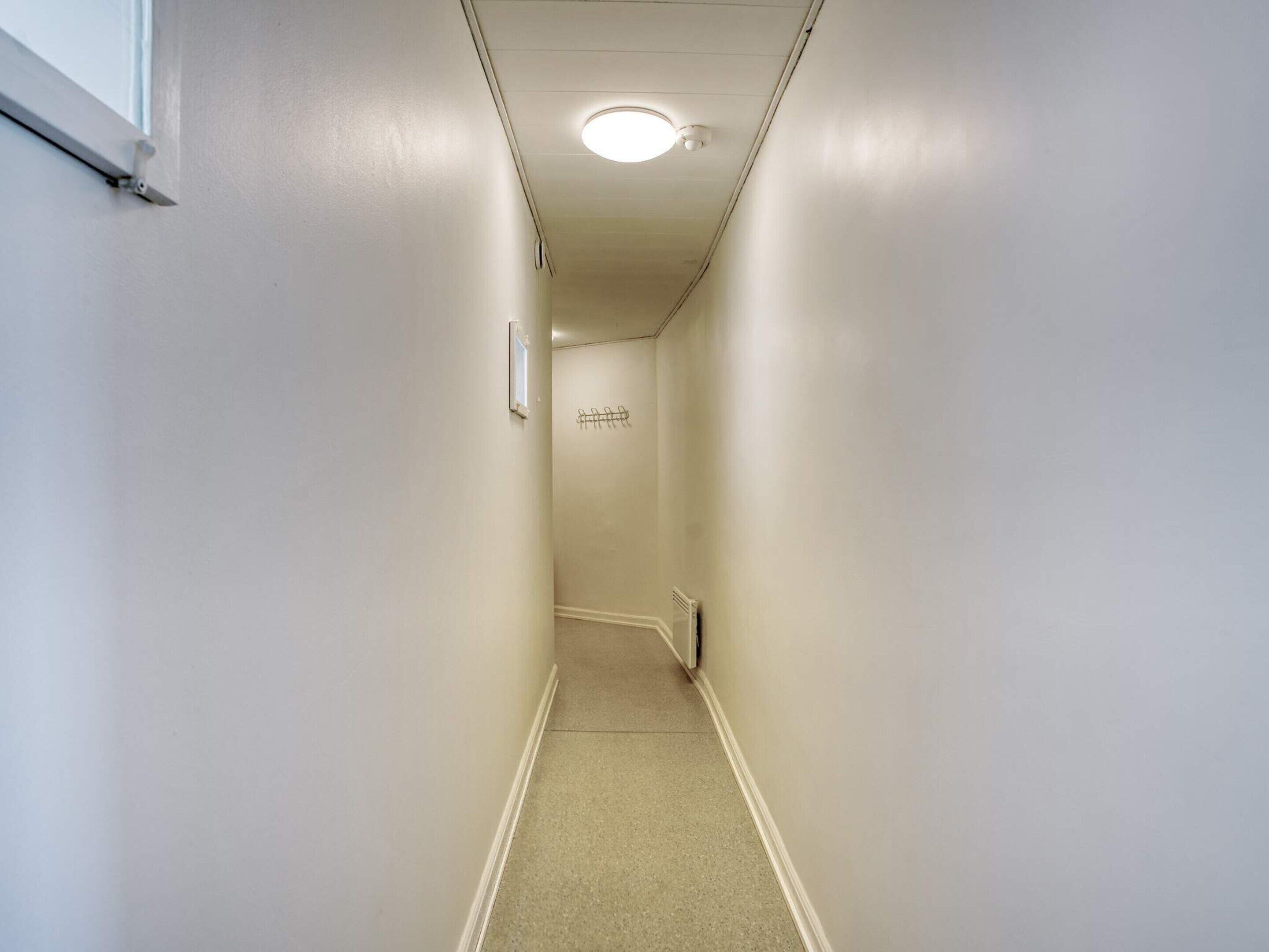 A narrow hallway with a white wall, a door at the end, and a ceiling light.