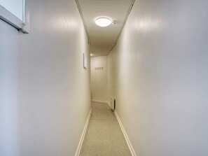 En smal hall med en vit vägg, en dörr längst in och en taklampa.