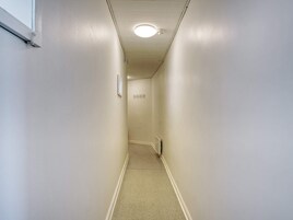 Un pasillo estrecho con pared blanca, una puerta al final y una luz en el techo.