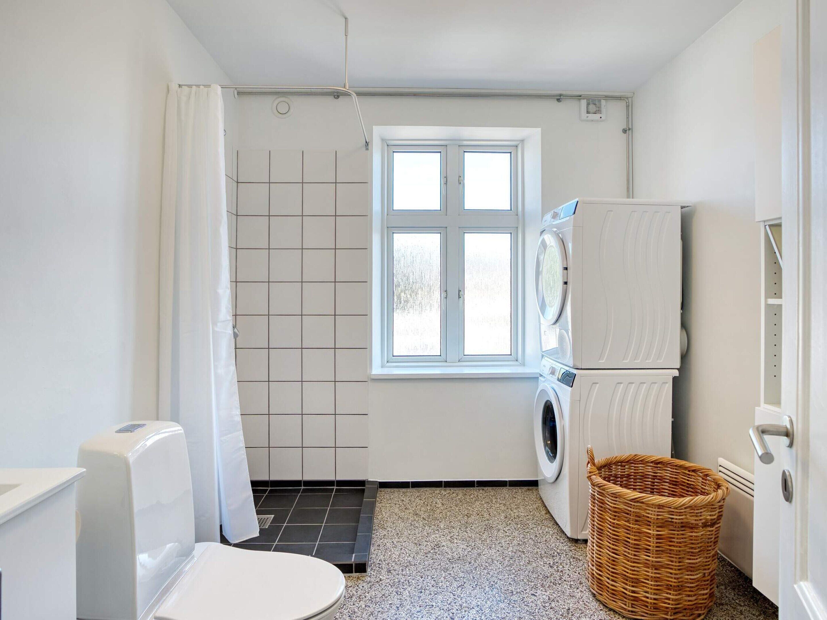 A compact laundry room with a washing machine, a dryer, a window, and a shower area.