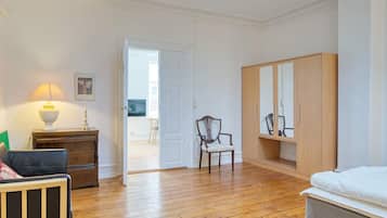 A bedroom with a wooden floor, a bed, a wardrobe, a chair, a desk, a lamp, and a door leading to a balcony.