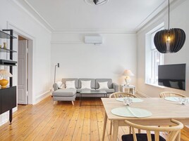 A modern living room with a grey sofa, a wooden dining table with chairs, a flat-screen TV, and a pendant light.