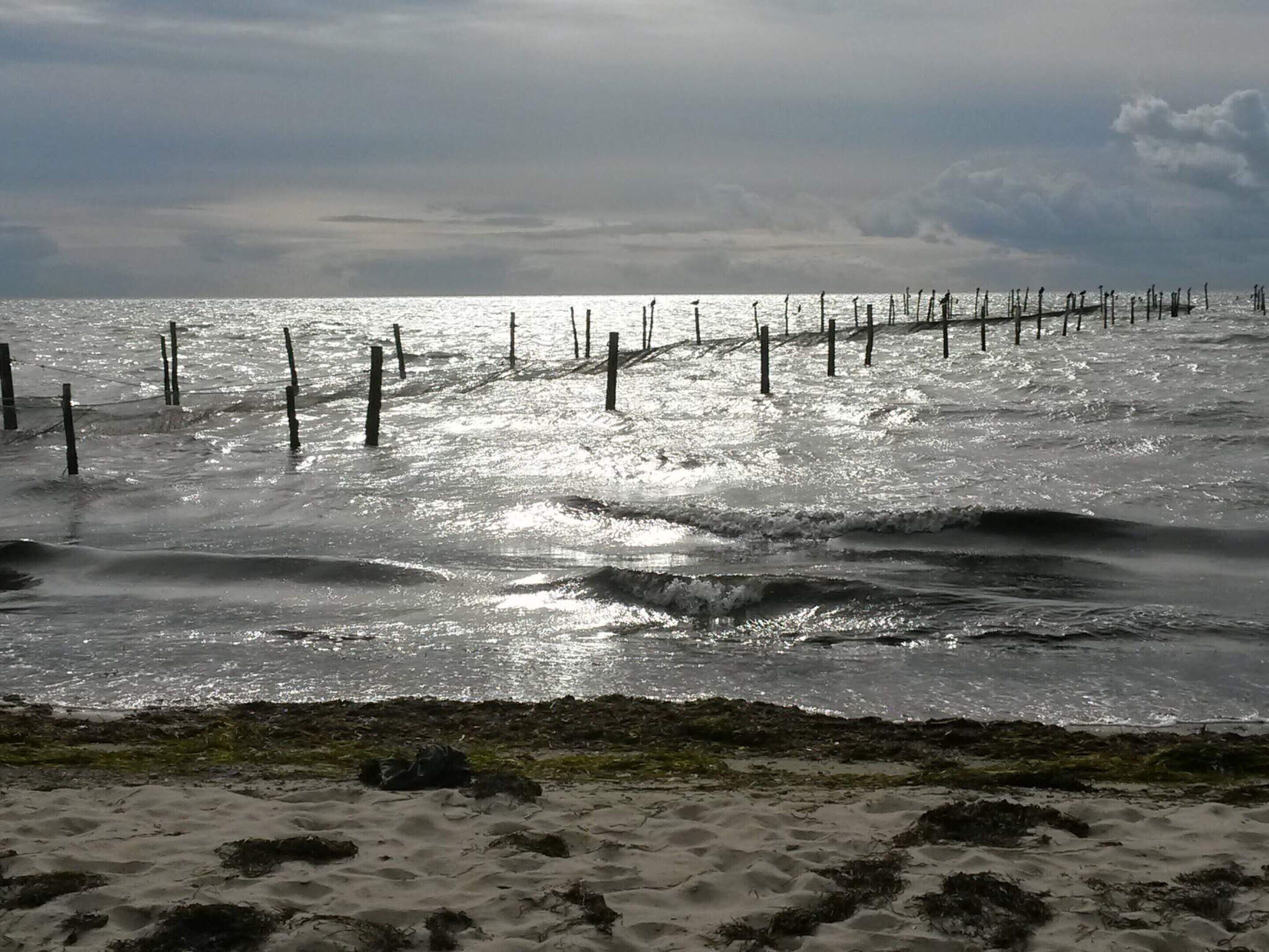Una spiaggia con una recinzione di legno e onde.