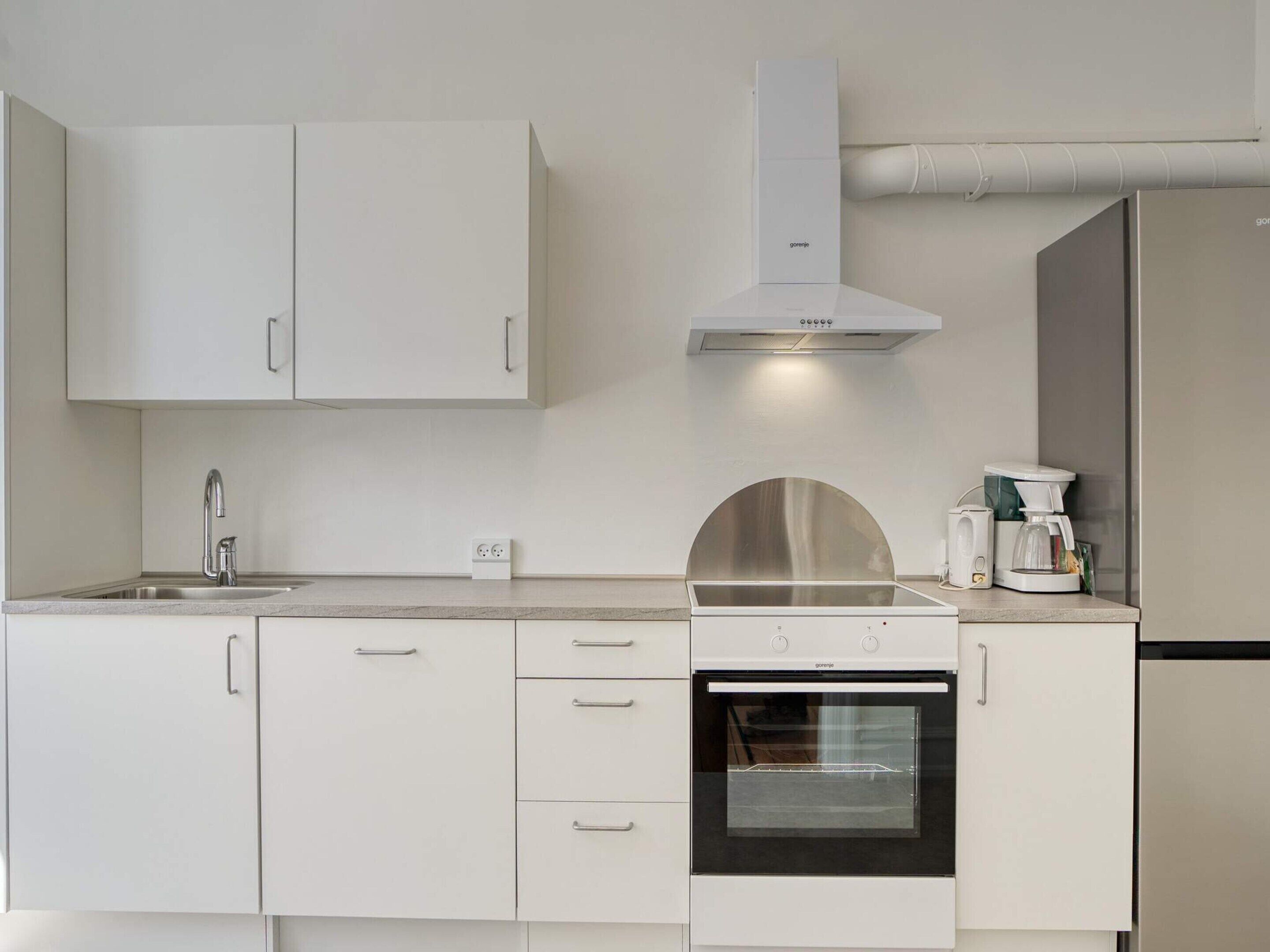 Una cocina moderna con armarios blancos, una campana de acero inoxidable, un horno empotrado y una cafetera.