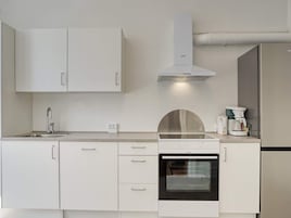 Una cocina moderna con armarios blancos, una campana de acero inoxidable, un horno empotrado y una cafetera.