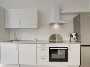 A modern kitchen with white cabinetry, a stainless steel range hood, a built-in oven, and a coffee maker. - 4 Person Holiday Home in Nakskov (Nakskov)
