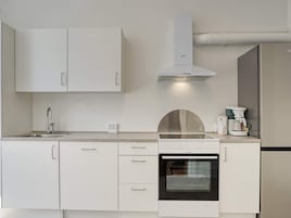 Una cocina moderna con armarios blancos, extractor de acero inoxidable, horno integrado y cafetera.