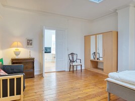 Una habitación con una cama, un armario de madera, una silla, un escritorio con una lámpara y una puerta que da a un espacio exterior.