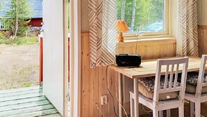 Una cabaña de madera con una mesa de comedor, sillas, un radio y una ventana con cortinas.