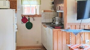 Cocina compacta con refrigerador, estufa y microondas. Hay una ventana con cortina, un armario de madera y un televisor montado en la pared.