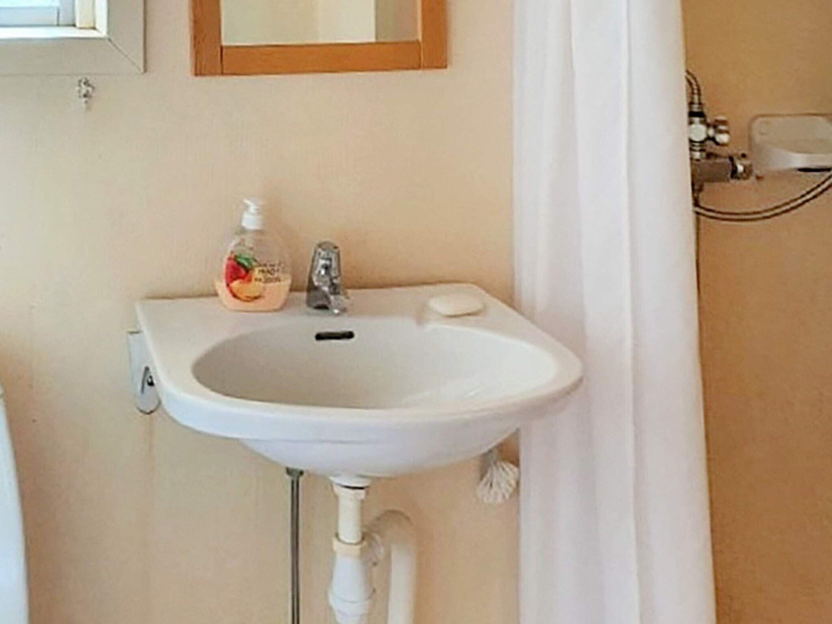 A bathroom with a white sink, a mirror above it, and a bottle of soap.