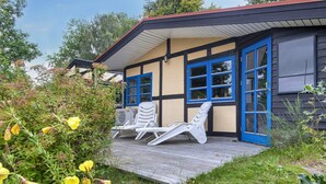 Un bâtiment doté d’une terrasse en bois, de deux fauteuils de jardin blancs et d’une porte bleue.