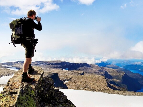 A person standing on a rocky outcrop with a backpack, overlooking a mountainous landscape with snow patches and a lake. - 6 Person Holiday Home in Svelgen-by Traum (Bremanger)