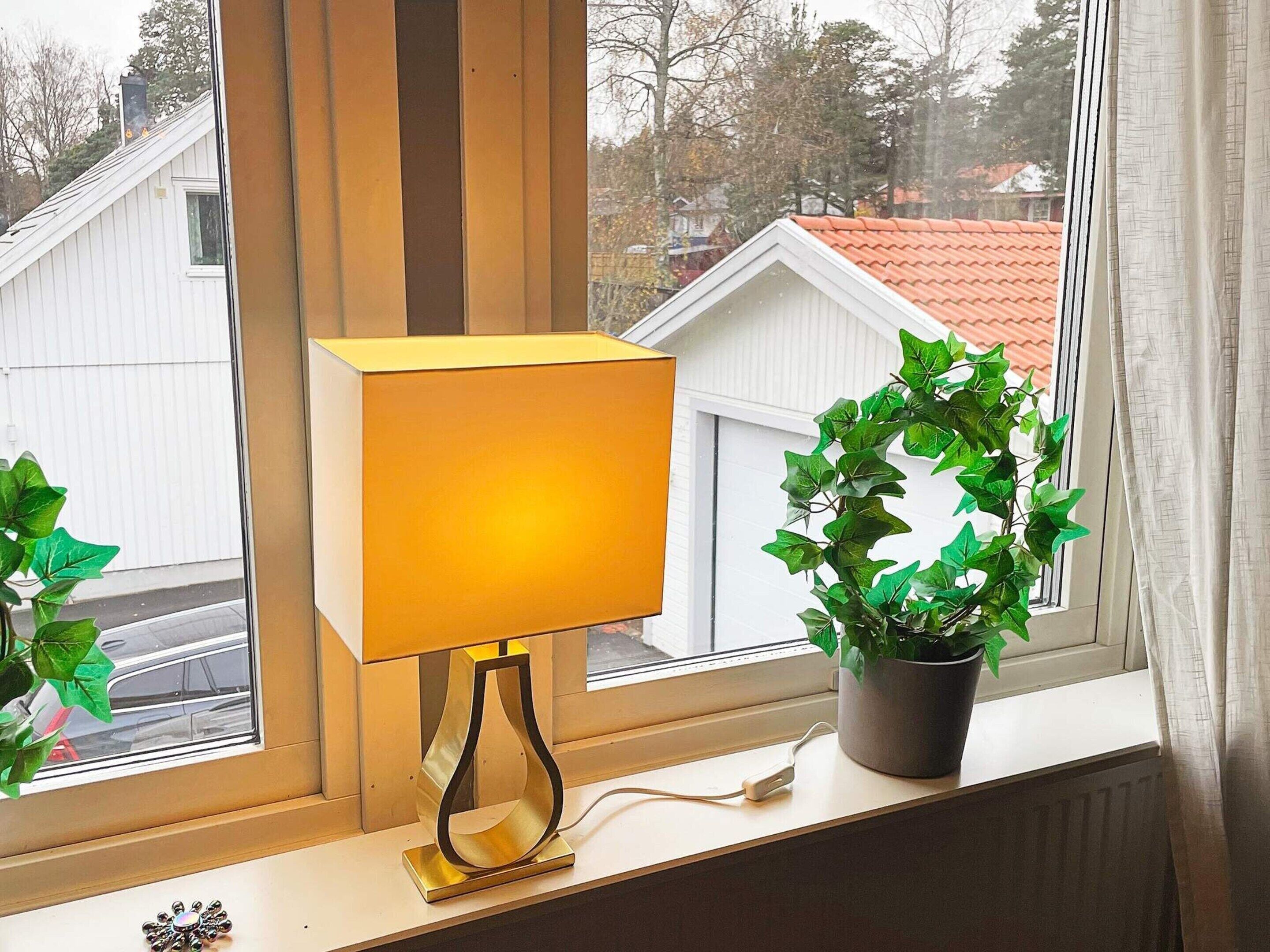 En lampa på en fönsterbräda med utsikt över hus och en växt.