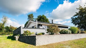 Une maison moderne à deux étages, avec une façade en briques, un toit plat et un petit jardin à l’avant, agrémenté d’un petit muret en briques et de quelques plantes.