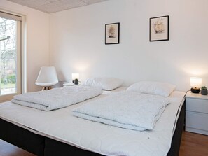 En dubbelsäng med vita sängkläder, två sängbord med lampor och två inramade tavlor på väggen.