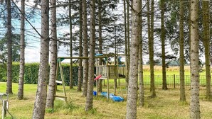 Un’area giochi con una struttura di legno per arrampicata e altalene, circondata da alberi.