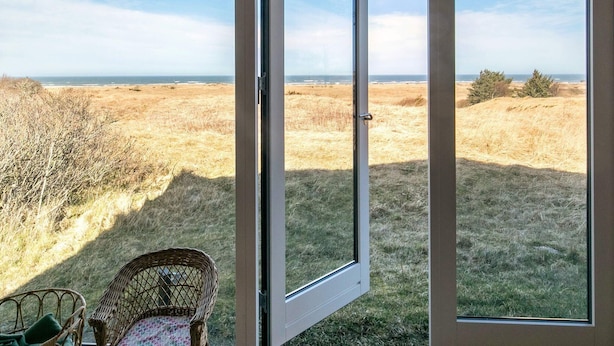 Una habitación con un amplio ventanal que da a un campo de césped y vista al océano.