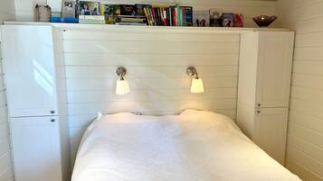 Un dormitorio con cama, un armario blanco, un mueble pequeño blanco y una estantería con libros y objetos decorativos.