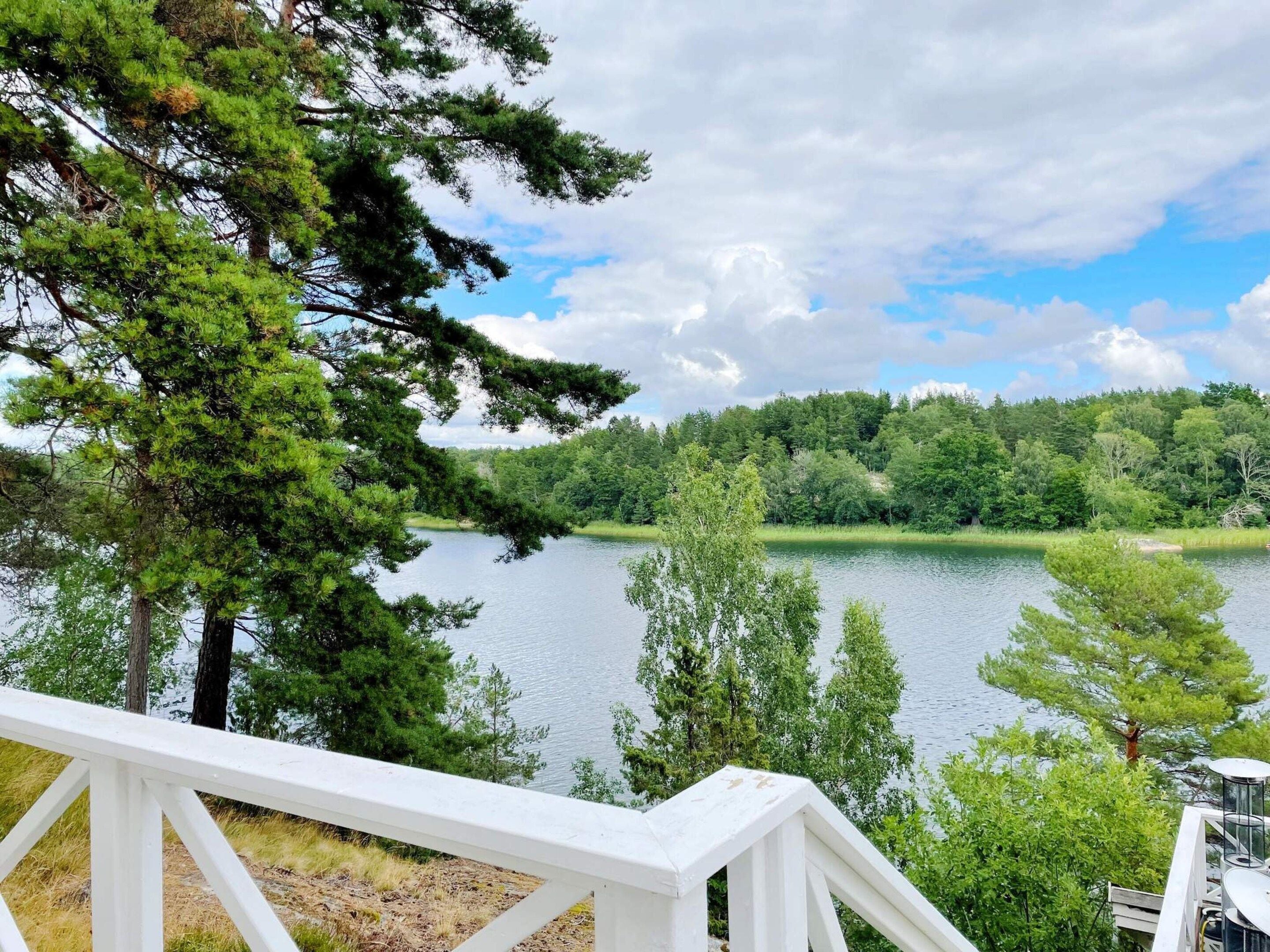 A lakeside view with a white deck overlooking a calm lake, surrounded by dense greenery and trees.