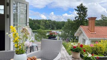 An outdoor patio with wicker furniture, a wooden table with a loaf of bread, and potted plants with flowers.