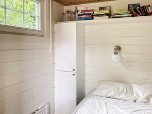 Et soveværelse med en seng, en radiator, et vindue og en bogreol fyldt med bøger.