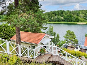 A wooden deck with a railing, overlooking a lake and a building with a red roof. - 4 Star Holiday Home in Ingaro (Ingaro)