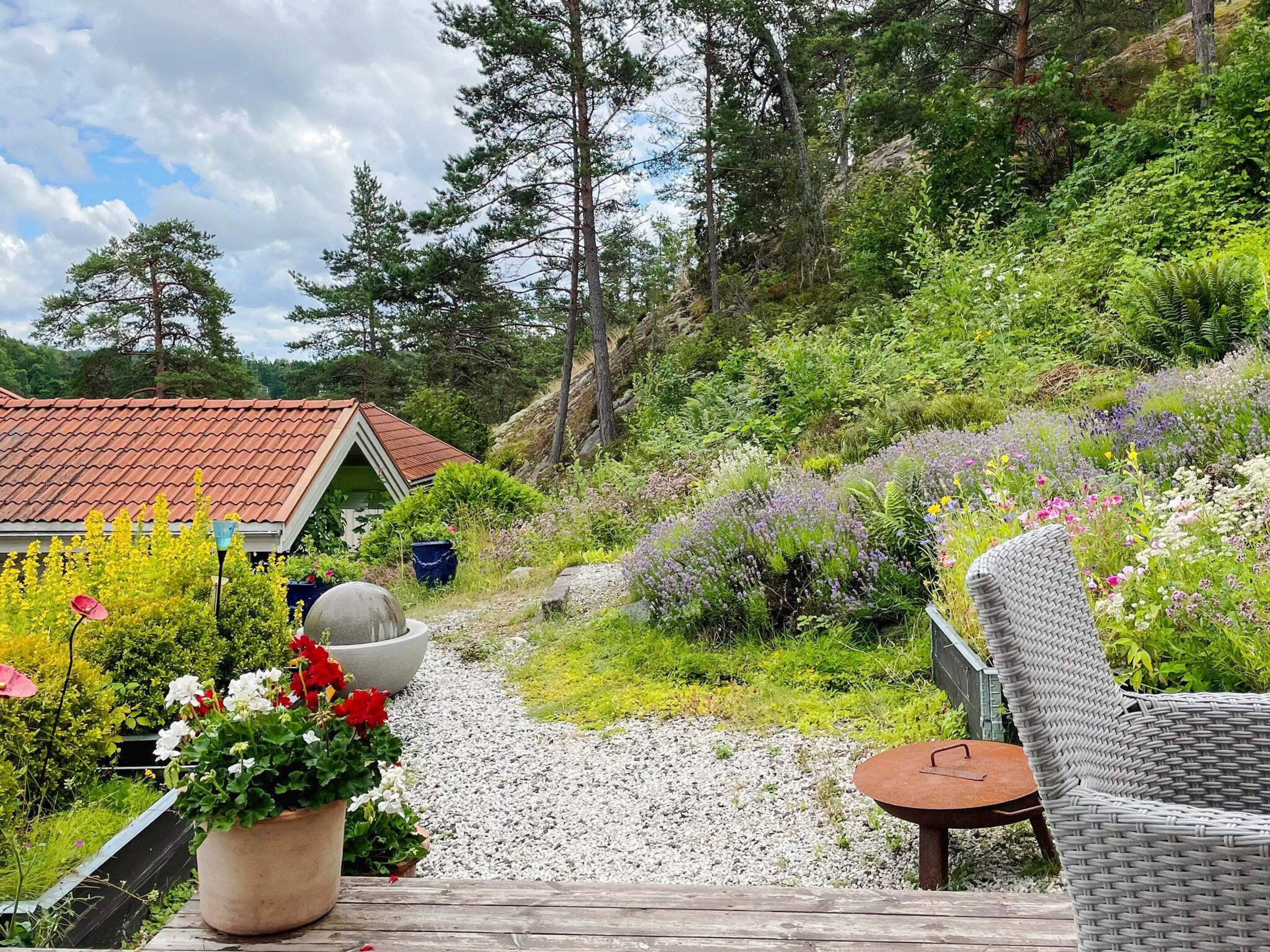 A garden area with a wooden deck, a wicker chair, and a potted plant with flowers.