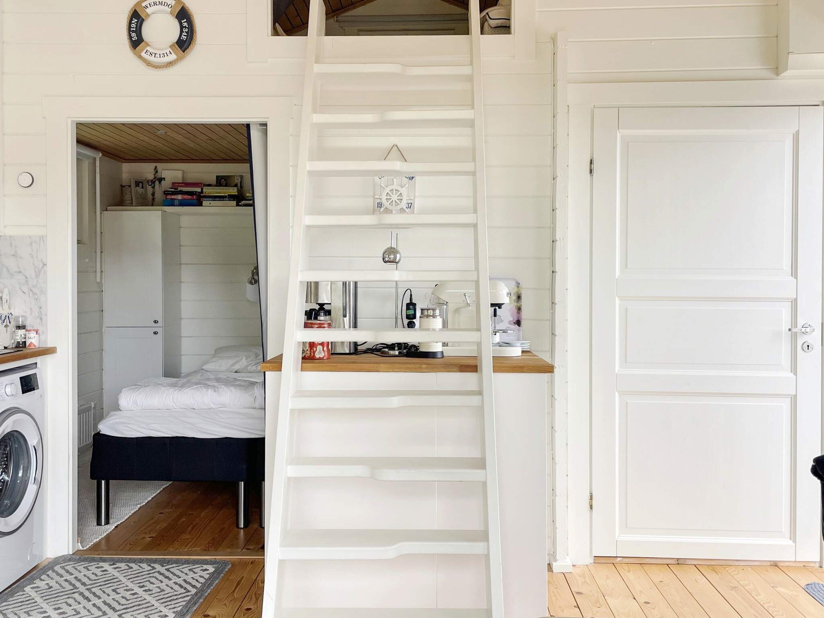 Habitación pequeña con cama, lavadora, kitchenette y puerta blanca.