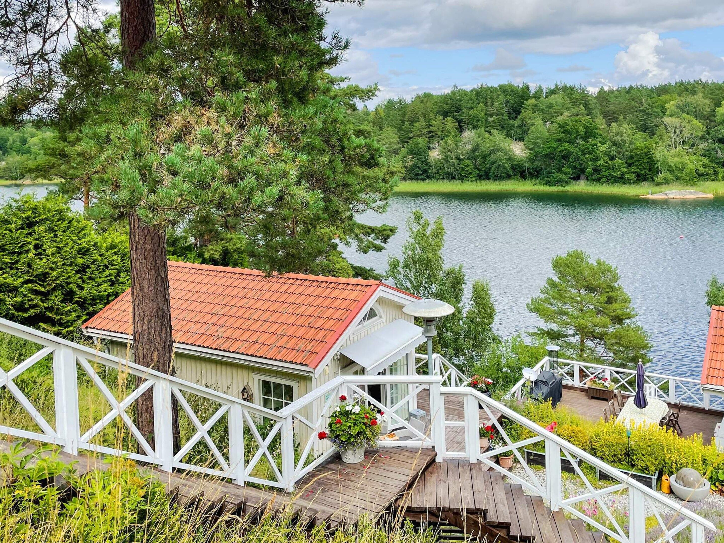 Eine Holzterrasse mit Geländer, mit Blick auf einen See und ein Gebäude mit rotem Dach.