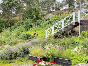 Eine Holztreppe führt einen Hügel hinauf, umgeben von üppiger Vegetation und verschiedenen blühenden Pflanzen.