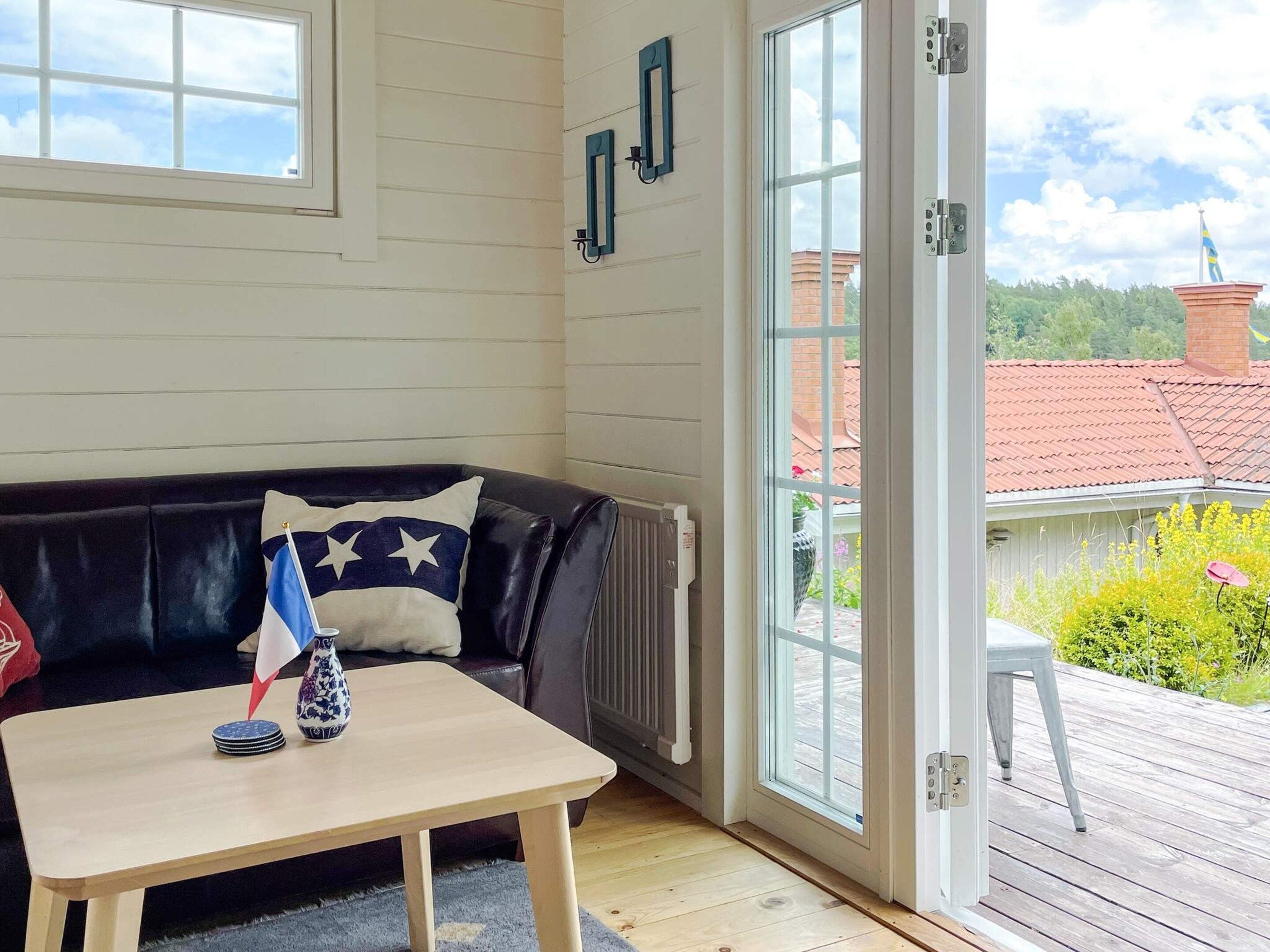A room with a black leather sofa, a small wooden table, and a view of a garden through a glass door.