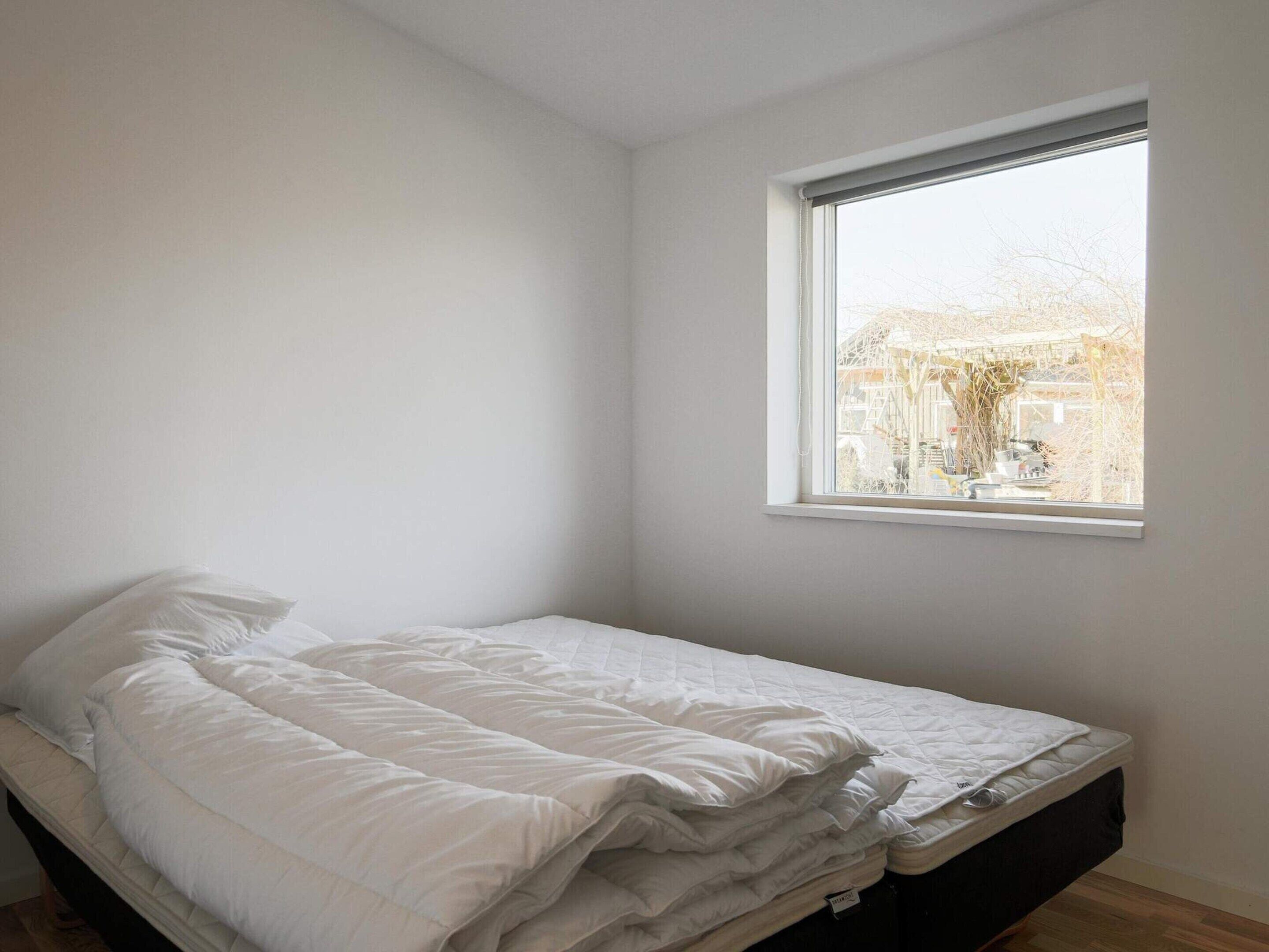 A small, single-bed room with a window overlooking a building.