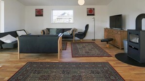En moderne stue med sofa, stol, fjernsyn, pejs og et vindue med udsigt til en bygning.