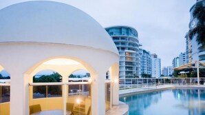 A modern hotel with a pool, featuring a curved building with arched windows and a poolside seating area. - ZANZIBAR APT 802- OCEAN VIEW APARTMENT (Mooloolaba)