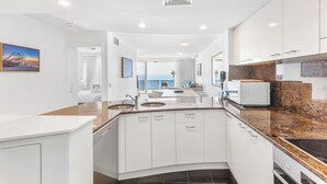 A modern kitchen with white cabinets, granite countertops, and a built-in oven. - ZANZIBAR APT 802- OCEAN VIEW APARTMENT (Mooloolaba)