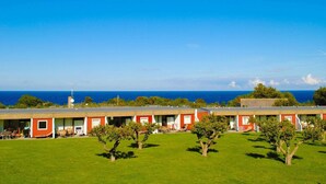 A row of red and white buildings with a grassy lawn in front, overlooking a clear blue sky and ocean. - 6 Person Holiday Home in Allinge (Allinge)
