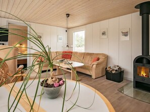 En hyggelig stue med sofa, sofabord, pejs og en potteplante.