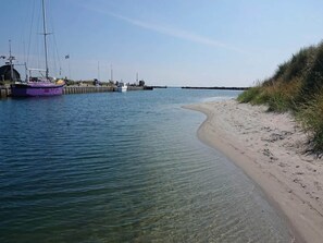A calm waterfront with a sandy beach and a dock with boats. - 8 Person Holiday Home in Hals (Hals)