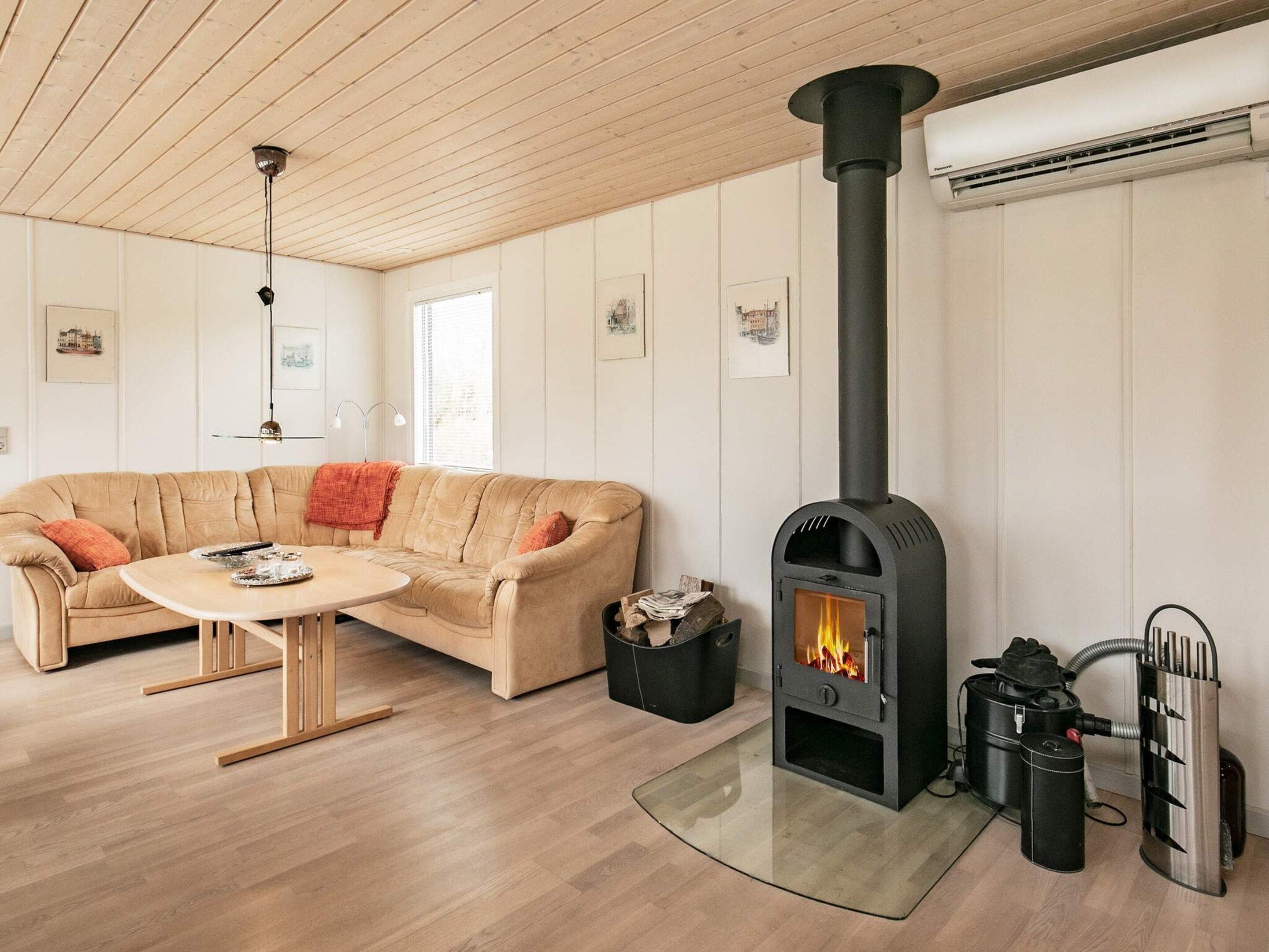 A cozy living room with a beige sofa, a round wooden coffee table, and a black wood-burning stove.
